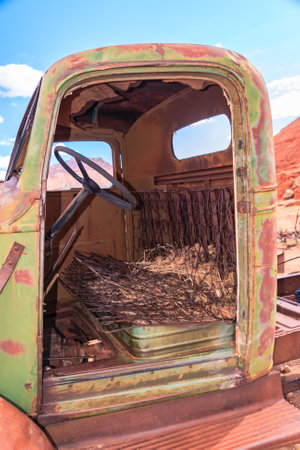 A green truck with a rusted interior. The interior is filled with hay and the truck is parked in a desertの写真素材