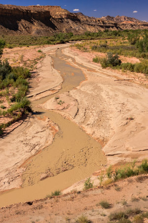 A river is flowing through a desert. The water is brown and muddy. The landscape is dry and barrenの写真素材