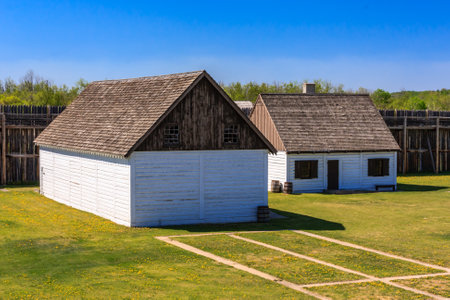 A white house with a slanted roof sits in a grassy field. The house is surrounded by a dirt road and a few trees. The scene has a peaceful and serene atmosphereの写真素材