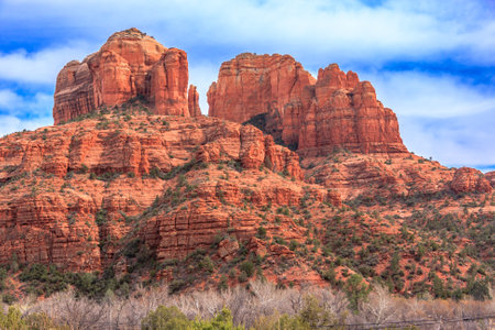 A beautiful mountain range with a mix of green and brown vegetation. The mountains are covered in red rocks, giving the scene a rugged and majestic appearance. The sky above is clear and blueの写真素材