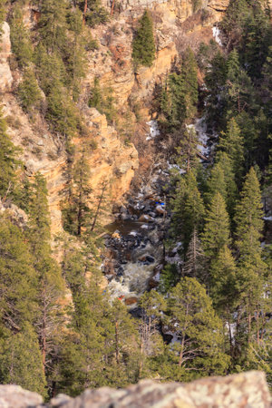 A mountain with a river running through it. The trees are green and the rocks are brown. The sky is blue and the sun is shiningの写真素材