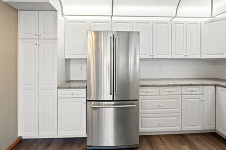 Stainless steel refrigerator is in a kitchen with white cabinets. The kitchen is clean and well-organizedの写真素材