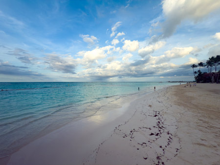 Beach with a clear blue sky and a few clouds. The beach is empty except for a few people walking along the shoreの写真素材