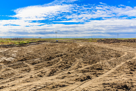 Dirt field with a few trees in the background. The sky is blue and there are some cloudsの写真素材