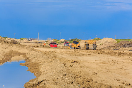 Construction site with a lot of dirt and a few cars. The cars are red and yellow
