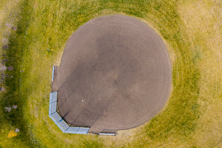 Baseball field with a dirt mound in the center. The mound is surrounded by a fence and grass