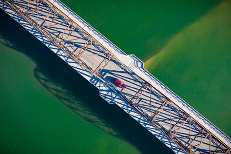 Bridge with a car on it. The bridge is over a body of water. The car is red