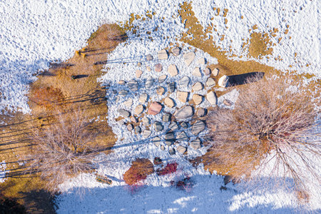 Snow covered landscape with a few trees and rocks. The snow is piled up in some areas and the ground...