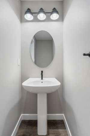 Small bathroom with a white sink and a mirror. The mirror is oval shaped and is located above the sinkの写真素材