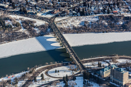 Bridge spans a river with a city in the background. The bridge is surrounded by snow and treesの写真素材