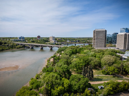 City view with a river running through it and a bridge over it. The bridge is in the middle of the river and is surrounded by trees. The city is full of buildings and the sky is clearの写真素材