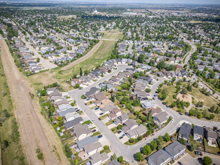 Residential neighborhood with houses and trees. The houses are mostly white and brown. There are cars parked on the street and a few people walking around. The sky is clear and the sun is shiningの写真素材
