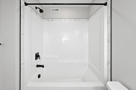 Clean and modern bathroom with a white bathtub and a black shower head. The shower head is mounted...