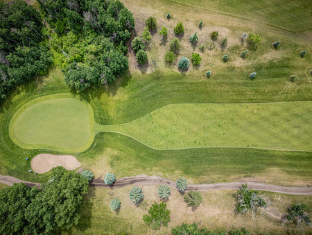 Golf course with a green grassy area and a sand trap. The grass is well-maintained and the trees are scattered throughout the courseの写真素材