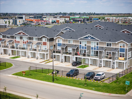 Row of apartment buildings with a green sign. The buildings are tall and have white roofs. There are several cars parked in the parking lot, including a black car and a white carの写真素材