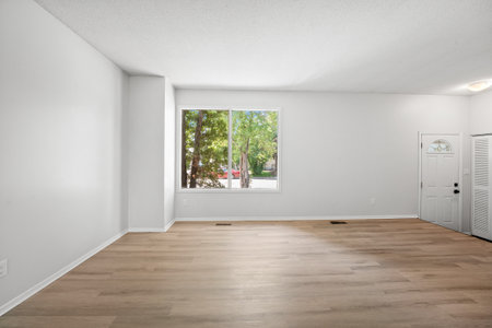 Large, empty living room with a window and a door. The room is very clean and has a very open feel...