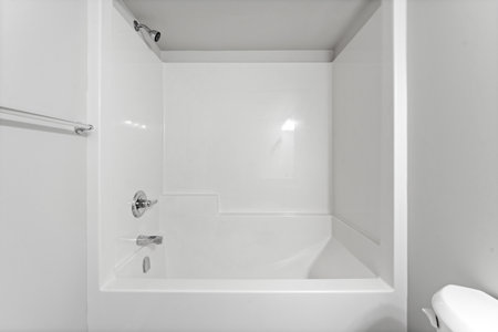Clean and empty bathroom with a white toilet and bathtub. The bathtub is positioned in the center of...