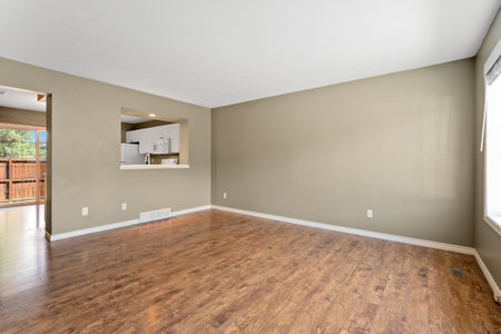 Large, empty living room with a kitchen area. The kitchen has a stove and oven. The room is very...
