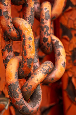 Chain with rusted links is shown in a close up. The chain is orange and has a worn appearanceの写真素材