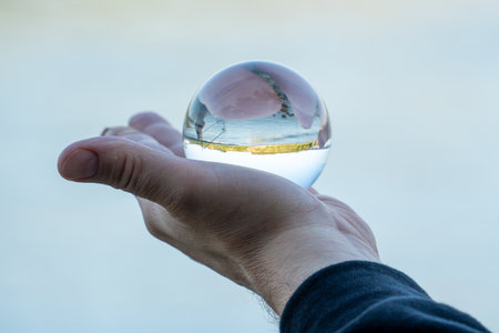 Person is holding a glass ball with a clear surface that reflects the sky. The reflection creates a serene and peaceful atmosphere, as if the person is holding a piece of nature in their handの写真素材