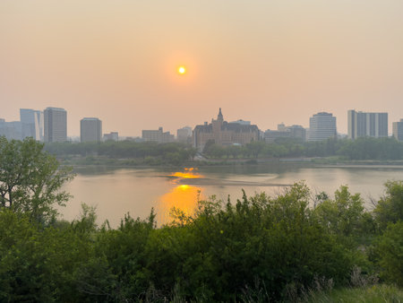 City skyline with a large building in the middle and a river running through it. The sun is setting, casting a warm glow over the sceneの写真素材