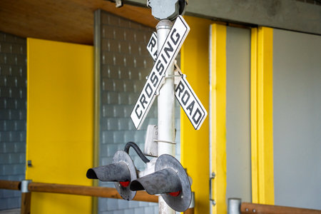 Railroad crossing sign is hanging from a pole. The sign is white and black. The pole is yellowの写真素材
