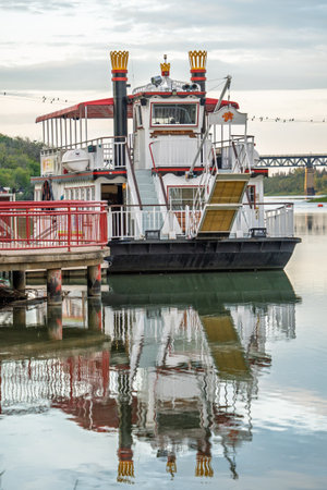 Large boat is docked at a pier. The boat is white and red and has a red railing around it. The water is calm and the sky is cloudyの写真素材