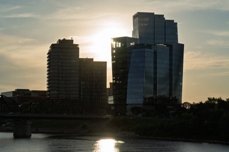 City skyline with a large building in the middle and a bridge in the background. The sun is setting, casting a warm glow over the sceneの写真素材