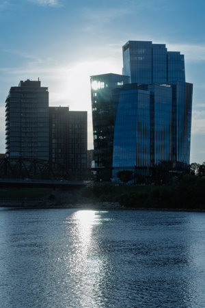 City skyline with a large building in the middle and a bridge in the background. The sun is shining on the water, creating a beautiful reflectionの写真素材