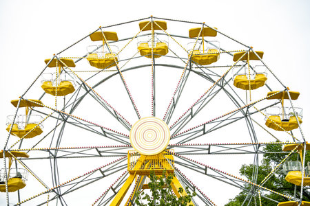 Yellow and white Ferris wheel with a red circle in the middle. The wheel is surrounded by trees and has many seatsの写真素材