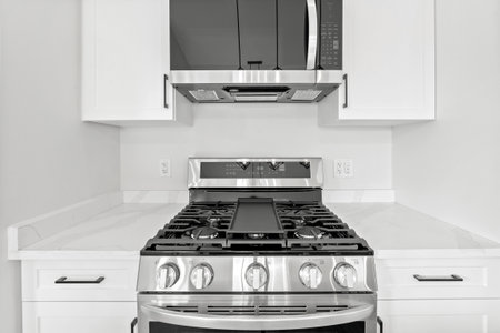 Silver stove with a black top. The stove has four burners and a black oven. The stove is in a white...