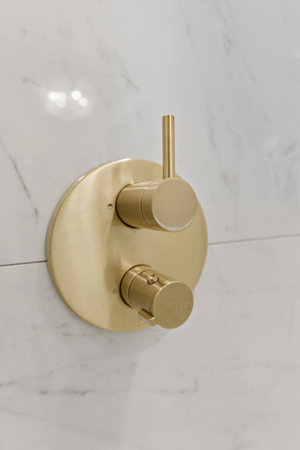 Gold faucet with a silver handle. The faucet is on a white wall