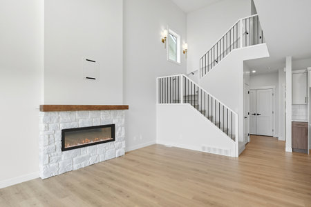 White fireplace with a mantel sits in front of a white staircase. The room is empty and has a lot of natural lightの写真素材