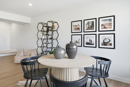 Black and white photo of a dining room with a round table and four black chairs. The table is surrounded by a rug and a white chair is placed in front of it. There are two vases on the tableの写真素材