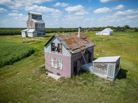Small house is in the middle of a field with a large grain silo in the backgroundの写真素材
