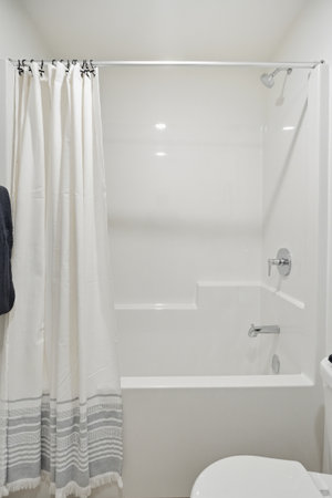 White bathroom with a shower curtain and a toilet. The shower curtain is white and has a black trim