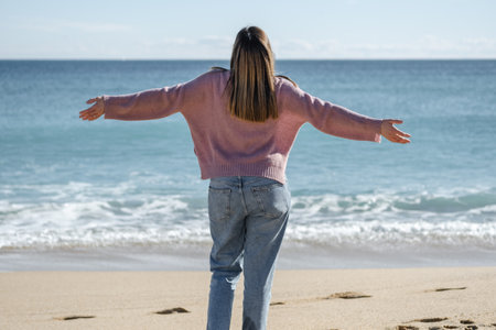 Clothed woman on the beach feeling free with her arms outstretched and looking towards the sky.の写真素材