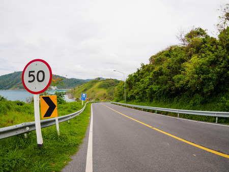 asphalt road on hill with limit speed sign board sea island at phuket Thailandの写真素材