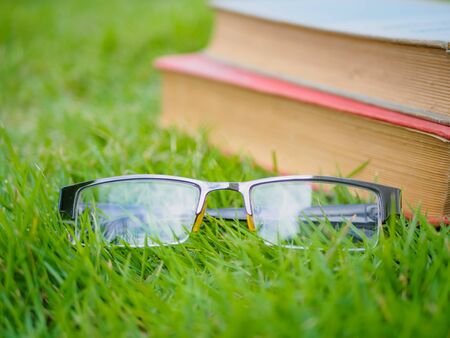 Old worn distressed vintage leather book and spectacles lying on lush green grass in summer sunshineの写真素材