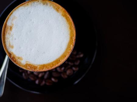 closeup cappuccino coffee on black cup with coffee bean on dark backgroundの写真素材