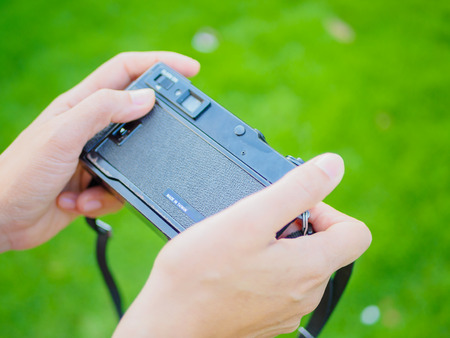 Pretty woman hand holding retro film camera with green grass field backgroundの写真素材
