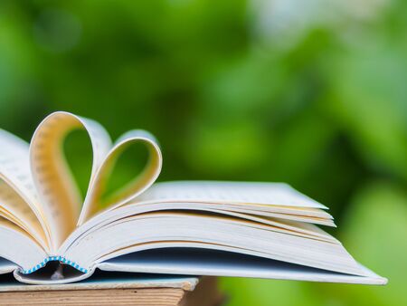 book on table in garden with top one opened and pages forming heart shapeの写真素材