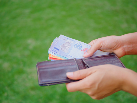 Women Hands taking out money malaysia ringgit from wallet on the green grass fieldの写真素材