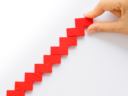 Concept of building success foundation. Women hand put red puzzle wooden blocks in the shape of a staircaseの写真素材