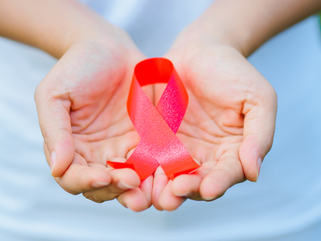 Red color ribbon awareness on young female woman girl teenager hand background: World aids day symbolic concept raising supportive help campaign public support people's health living with HIV, STDの写真素材