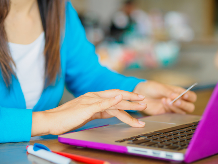Pretty Young womans hands holding a credit card and using laptop computer for online shopping. Online payment. Female working on laptop in a cafe.の写真素材