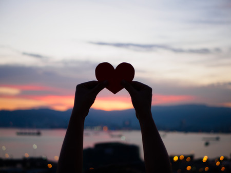 silhouette hand is raising the red paper heart with blur sunlight during sunset, Valentines dayの写真素材