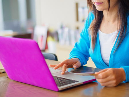 Pretty Young womans hands holding a credit card and using laptop computer for online shopping. Online payment. Female working on laptop in a cafe.の写真素材