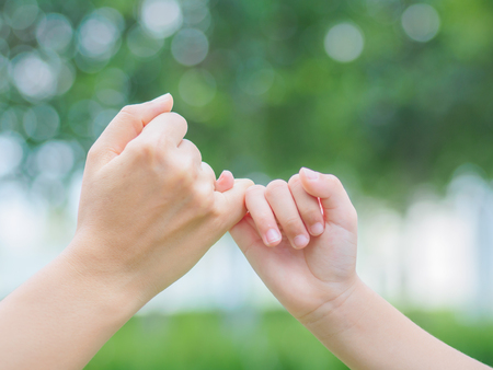 Mother holding a hand of her kid in spring day outdoors with green field backgroundの写真素材
