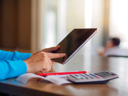 Pretty Young womans hands holding and using tablet for online shopping, bill, pencil and calculator on the table. Online payment. Female working on tablet in a cafe.の写真素材